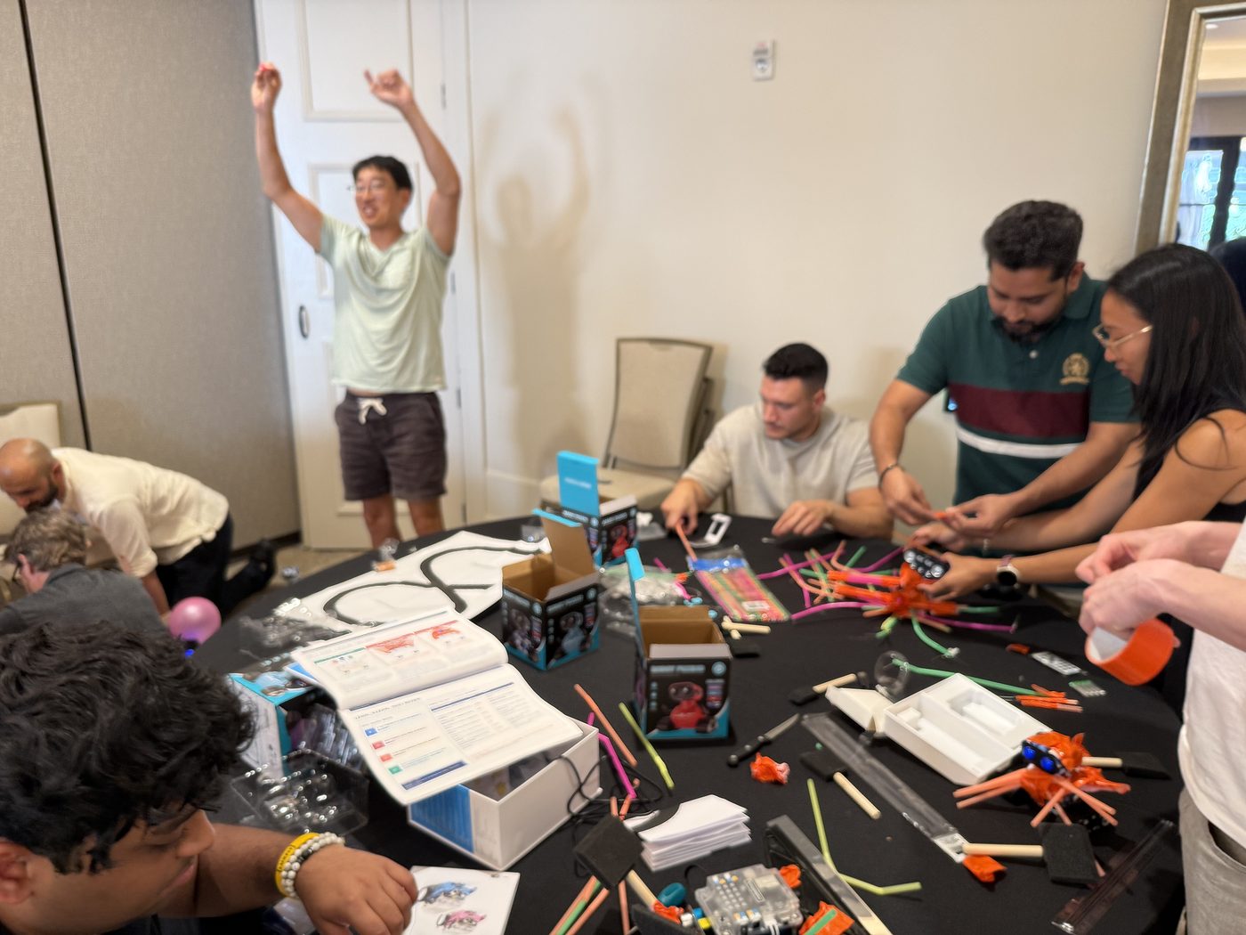A teammate raises his arms in celebration while coworkers work on their robot